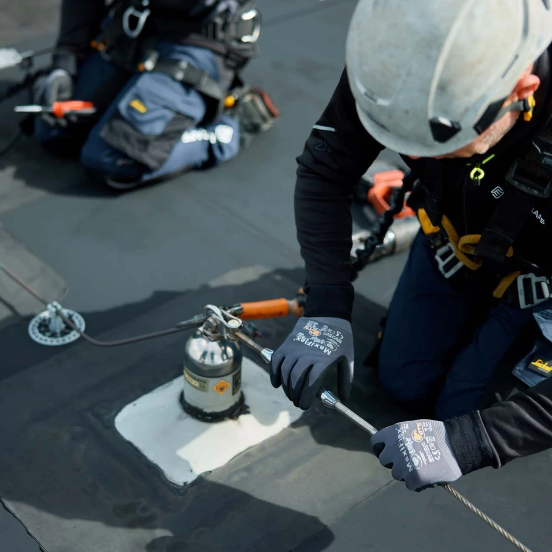 mannen op plat dak met helm op en harnas aan bezig met ankerpunten