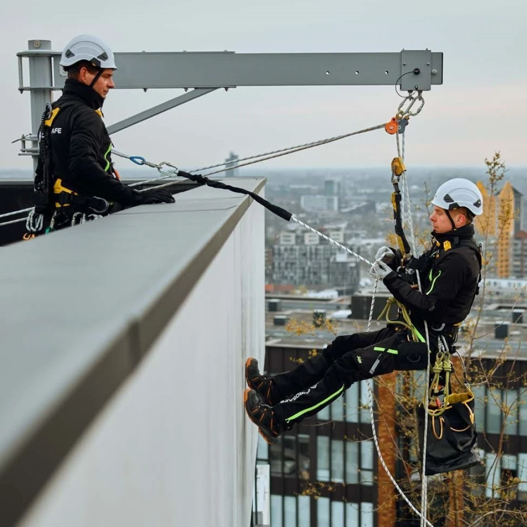 twee mannen op hoog dak met beveiliging man hangt aan dak