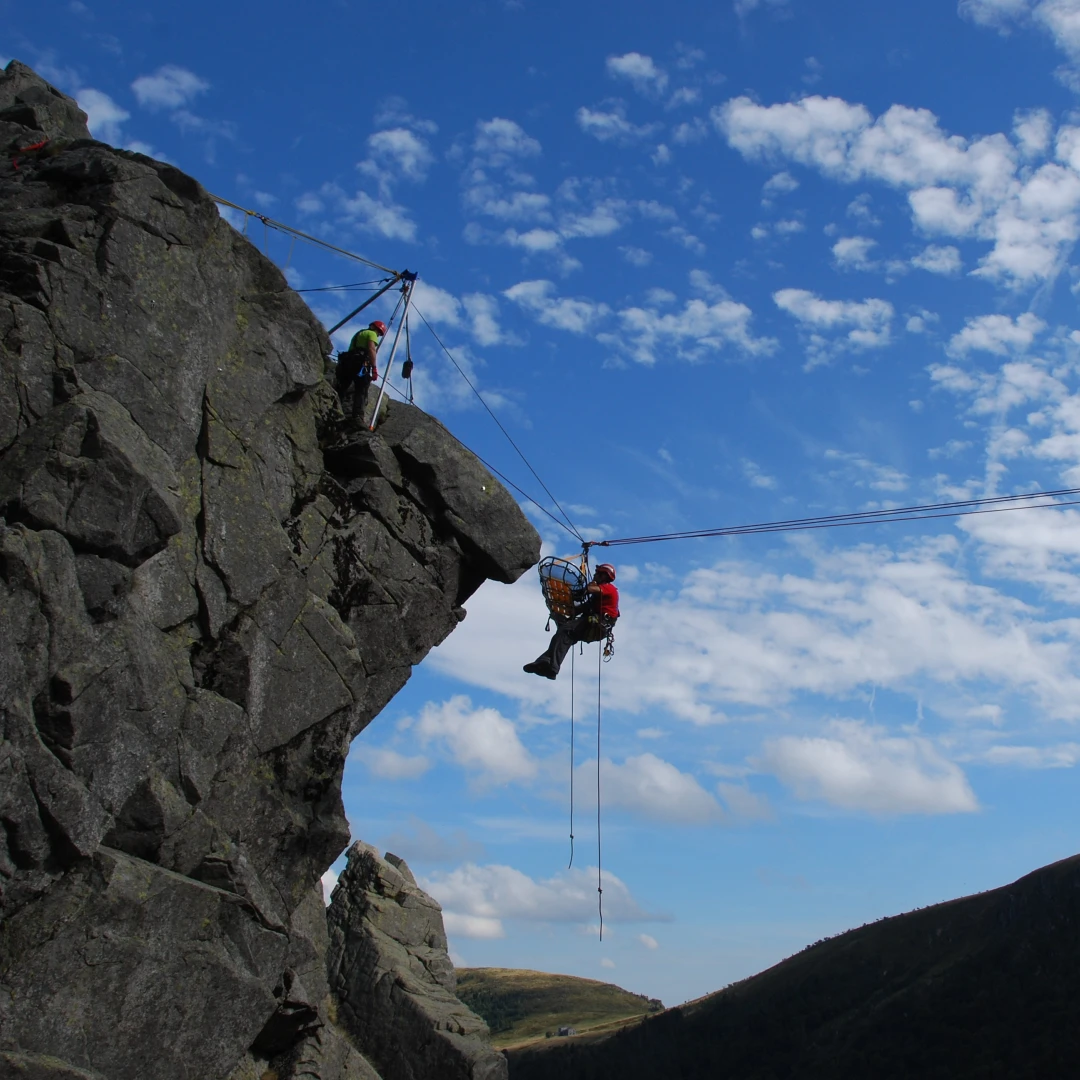 grote rots met man hangend in touw met helm en brancard
