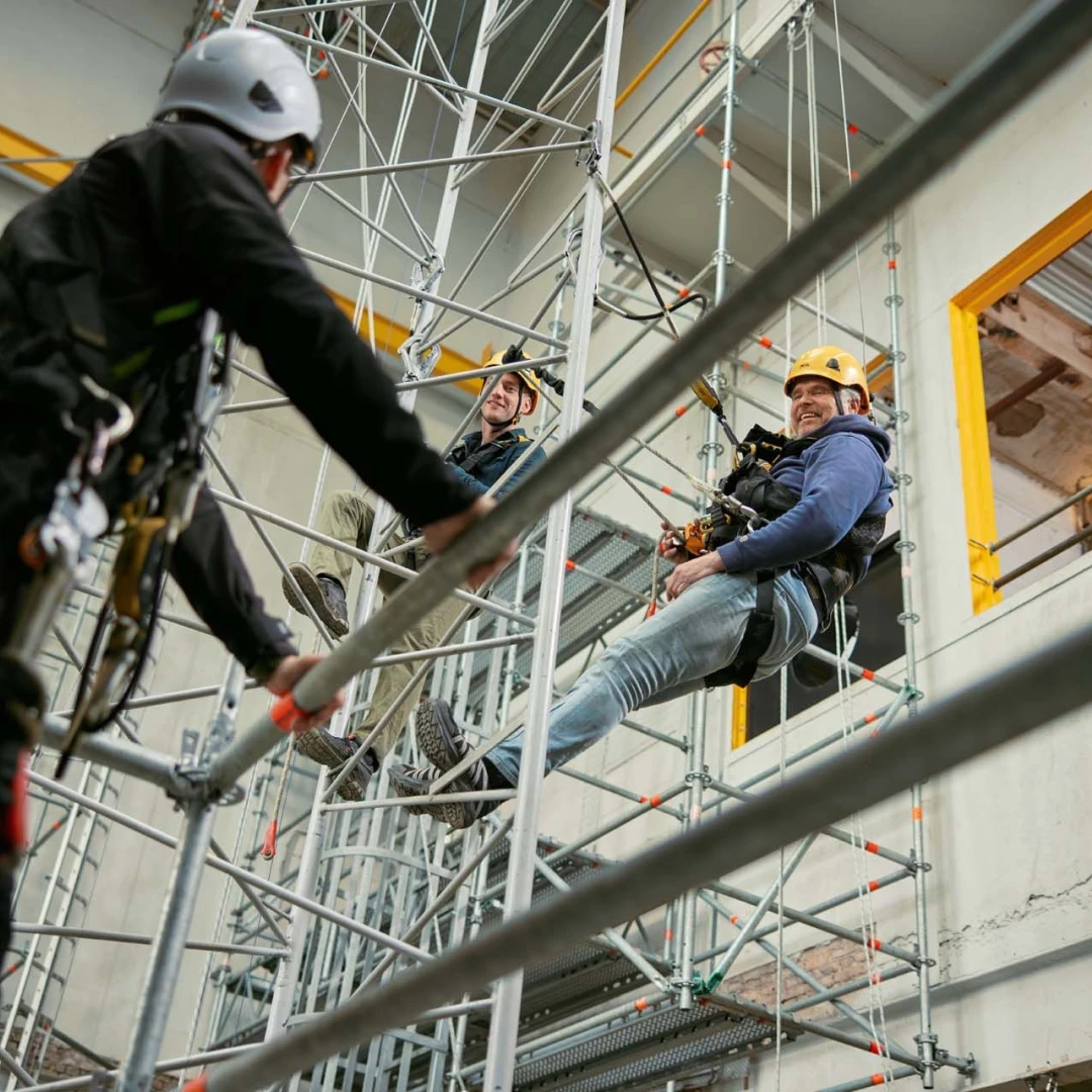 lachende man hangend aan touw met harnas op hoogte in loods