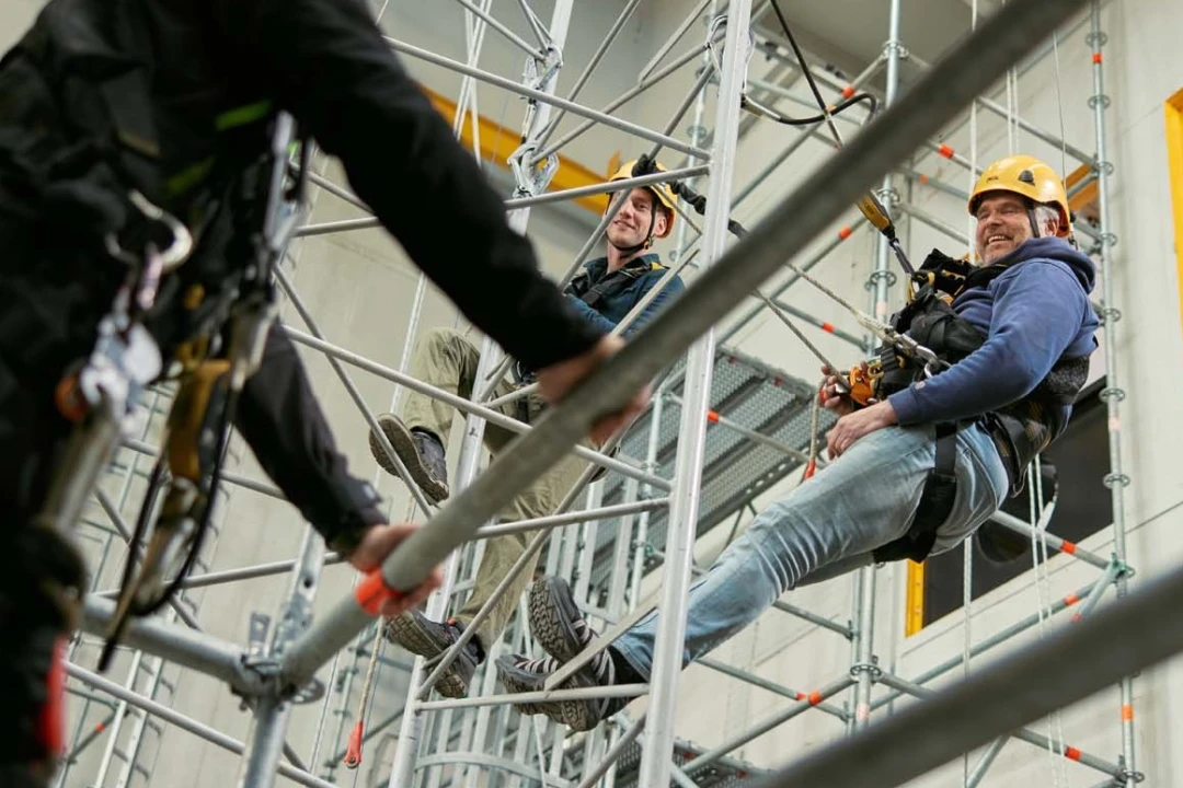 personen op hoogte hangend aan touw met helm op en harnas aan