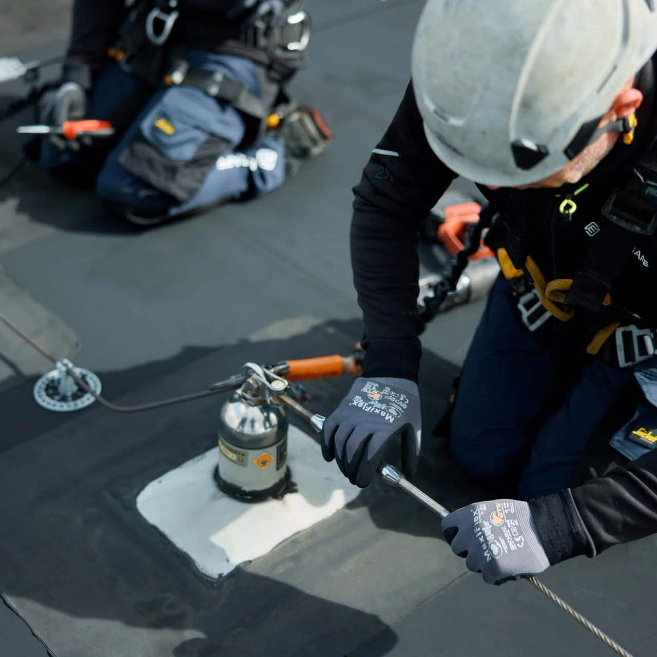 mannen op plat dak met helm op en harnas aan bezig met ankerpunten