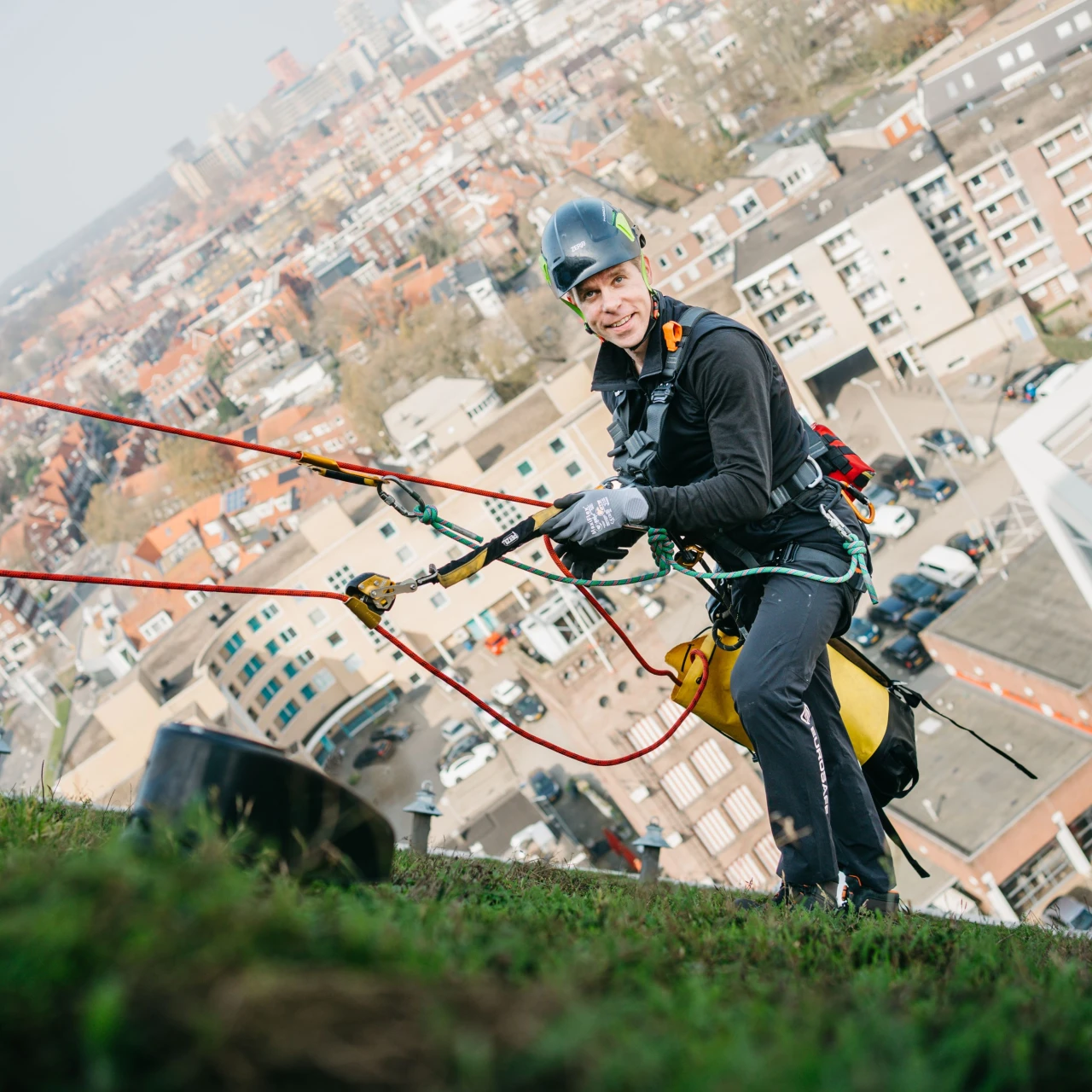 man staat op een hellend groendak aangelijnd