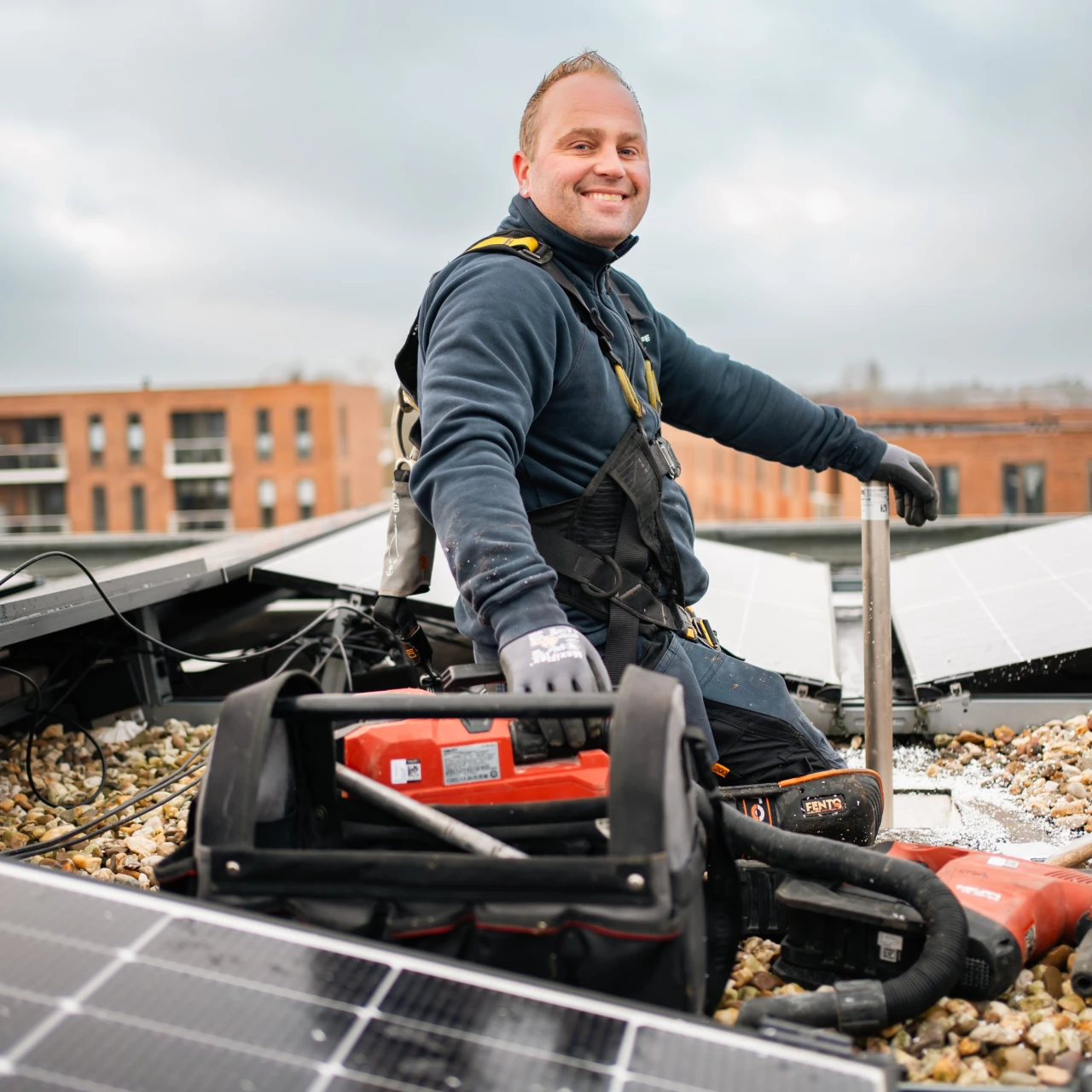 een man die op een dak zit met een gereedschapskist