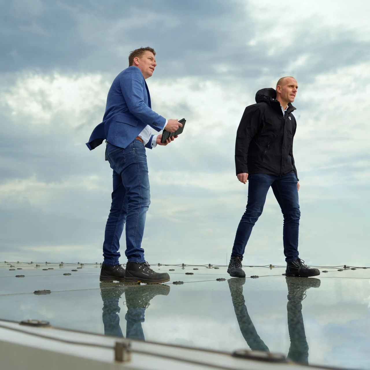 twee mannen die staan op een glazen dak met een jas aan