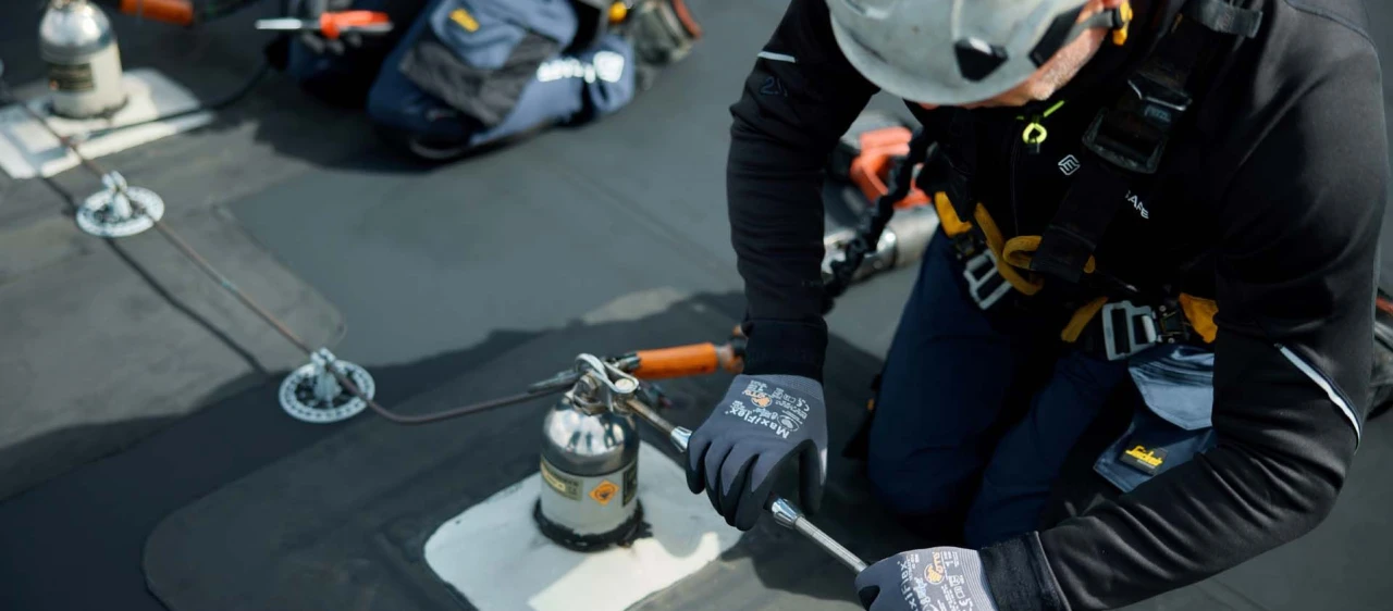 mannen op plat dak met helm op en harnas aan bezig met ankerpunten