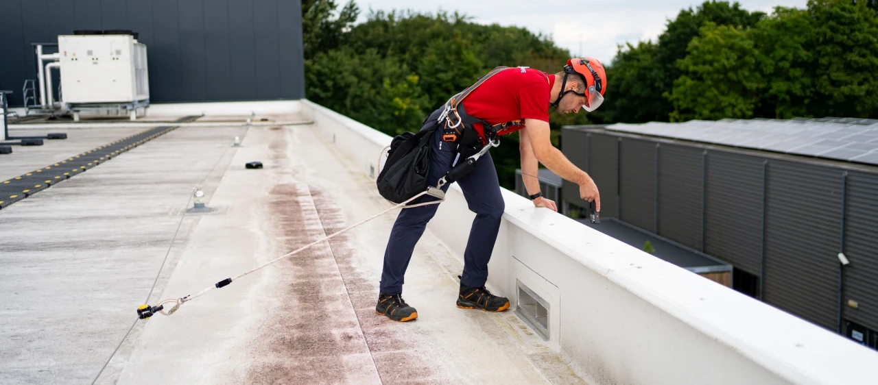 een man die staat op een plat dak met persoonlijke beschermingsmiddelen aan