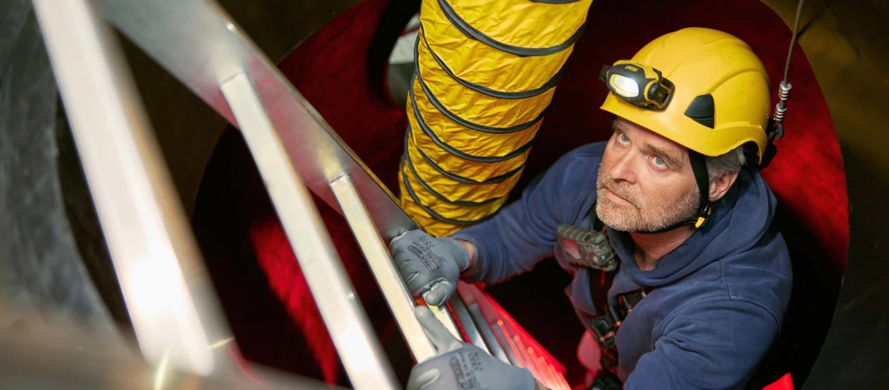 man op ladder in besloten ruimte met helm en lamp op hoofd