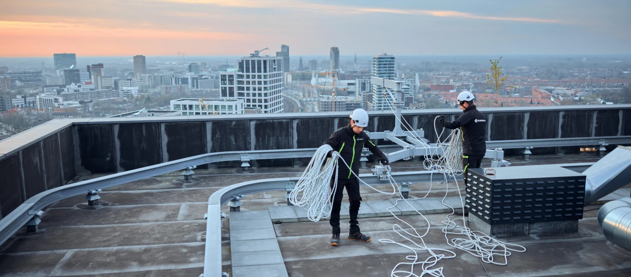mannen op hoog dak met helm op en touw vast