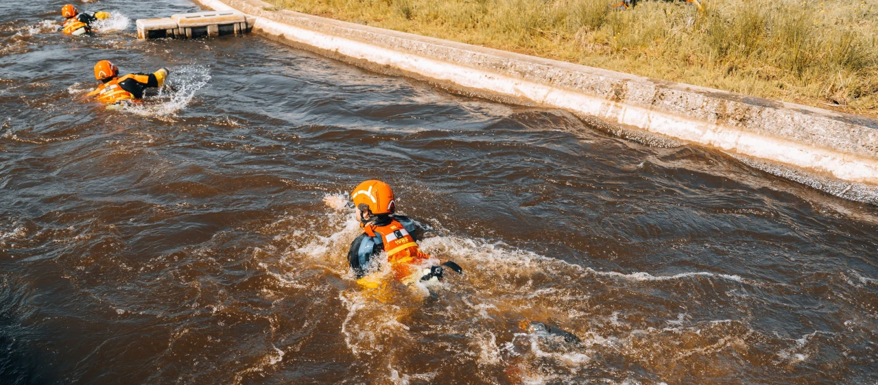 drie personen in snel stromend natuurwater die zichzelf proberen te redden