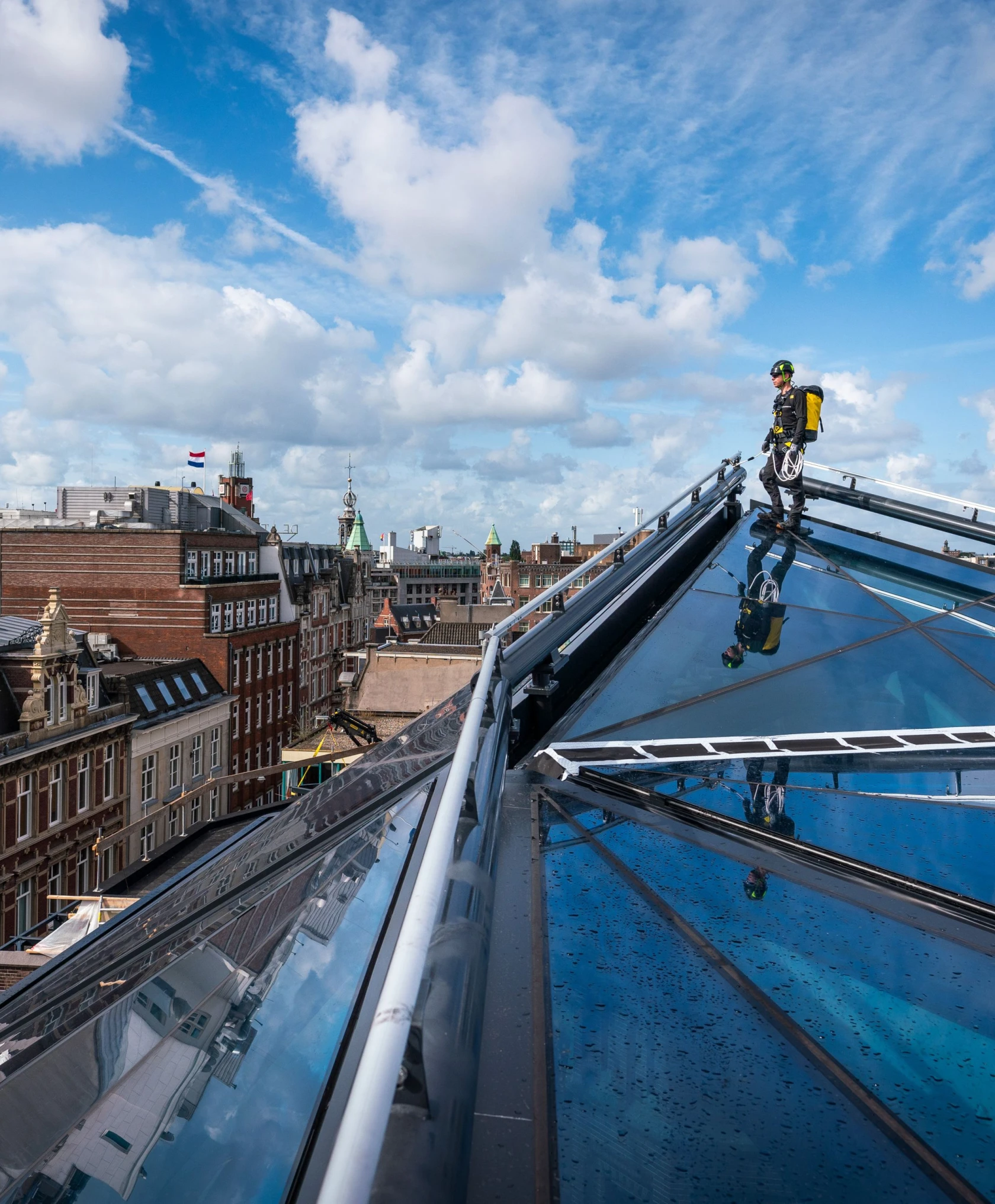 een man die op een glazen dak staat aangelijnd aan een railsysteem, geheel op maat gemaakt