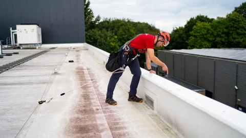 een man die staat op een plat dak met persoonlijke beschermingsmiddelen aan
