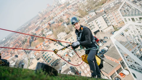 man staat op een hellend groendak aangelijnd