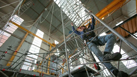 man die ladder beklimd in loods met helm en harnas
