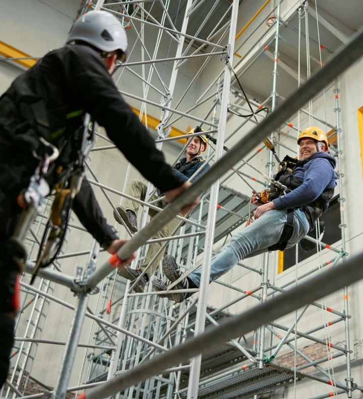 personen op hoogte hangend aan touw met helm op en harnas aan