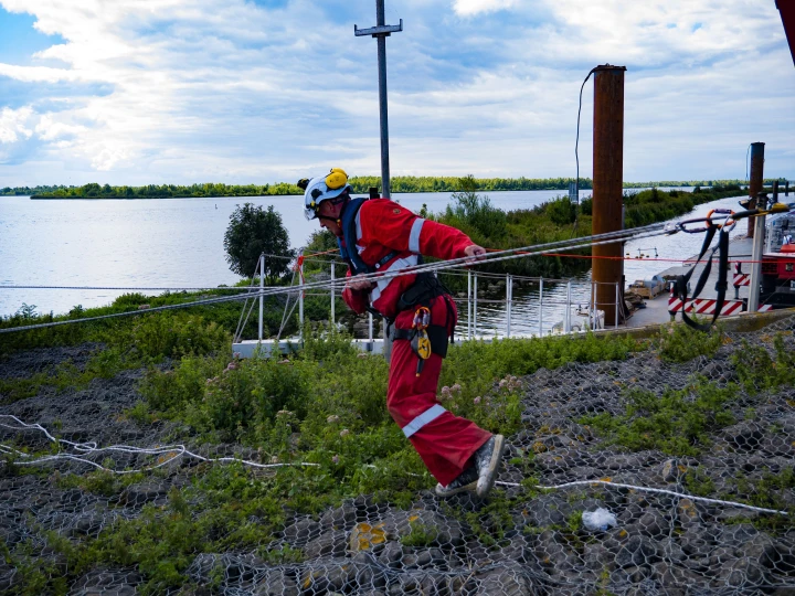 man met helm en reddingsvest bij haven en hij loopt langs touw