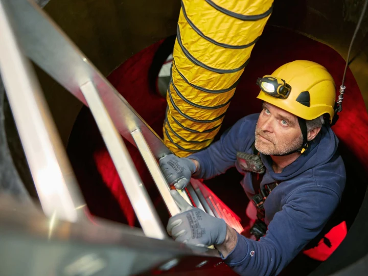 man op ladder in besloten ruimte met helm en lamp op hoofd