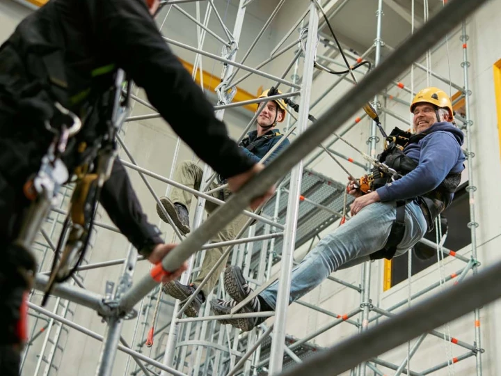 personen op hoogte hangend aan touw met helm op en harnas aan