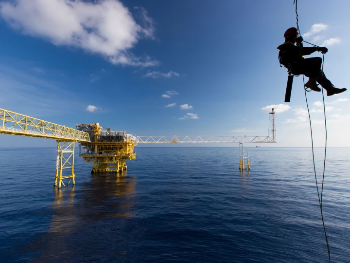 man aan touw hangend bij water met helm