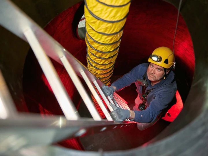 man met helm en lamp op hoofd klimmend op trap in besloten ruimte