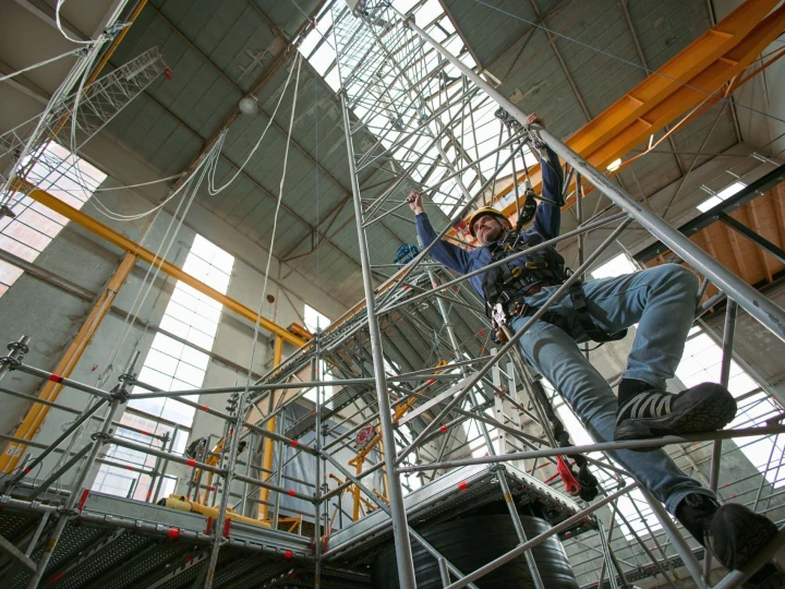 man op trap in loods met harnas en helm